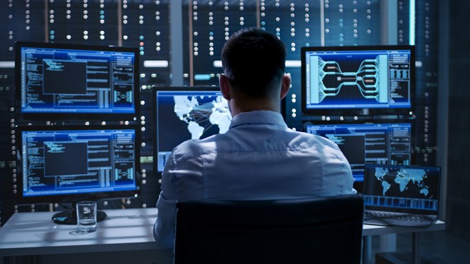 An analyst reviewing data and a world map across a wall of screens in an operations centre.